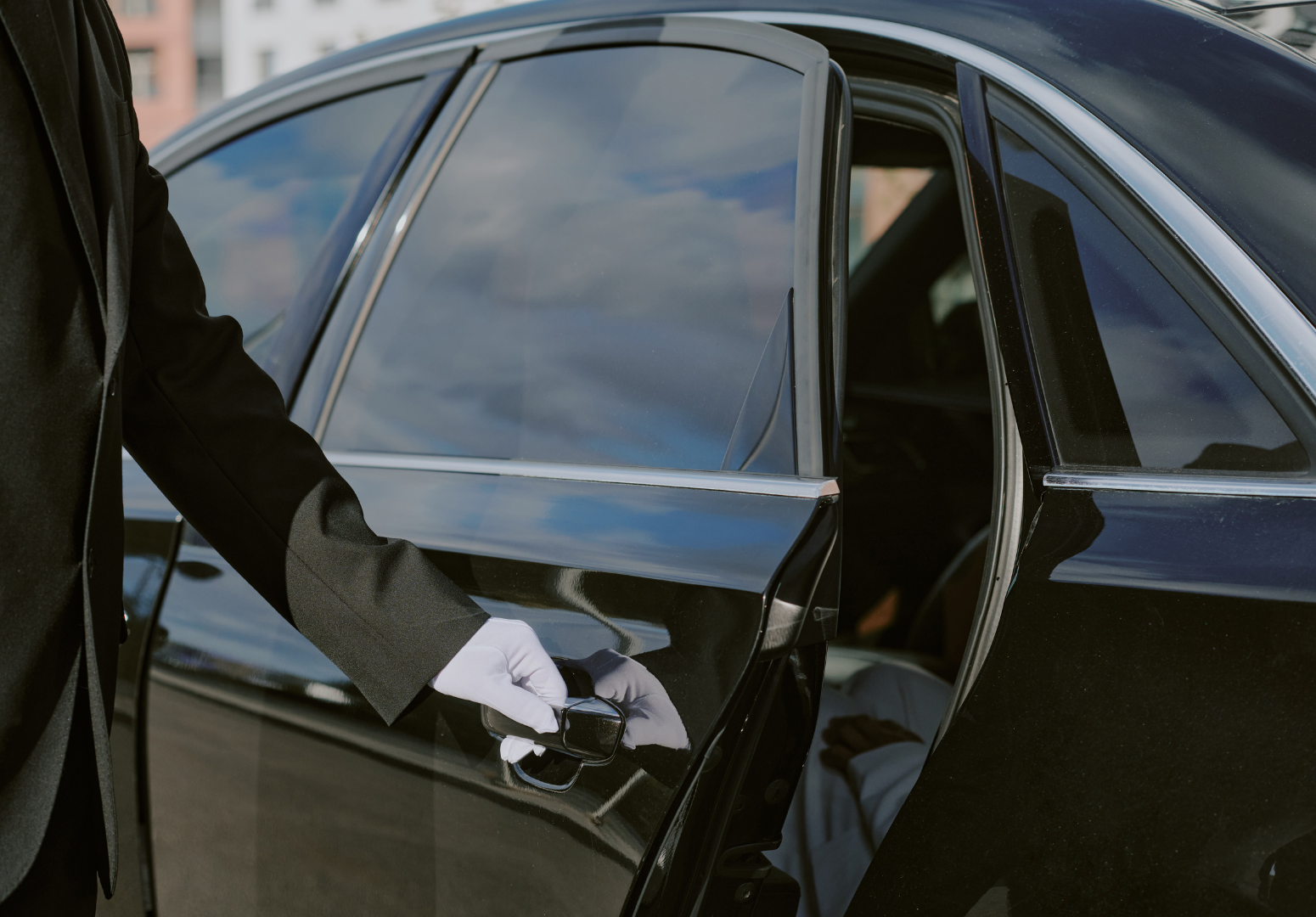 A driver opening the door for an executive about to exit a black car